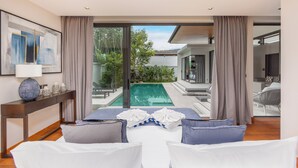 A modern hotel room with a bed, a desk, a lamp, and a view of an outdoor swimming pool. - Exclusive Magnum Villa With Private Pool (Si Sunthon)