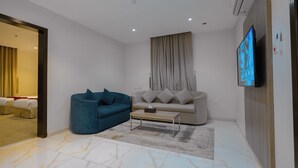 A modern living room with a sofa, a blue armchair, a coffee table, and a flat-screen TV mounted on the wall. - Akarem Jazan Serviced Apartments (Jizan)