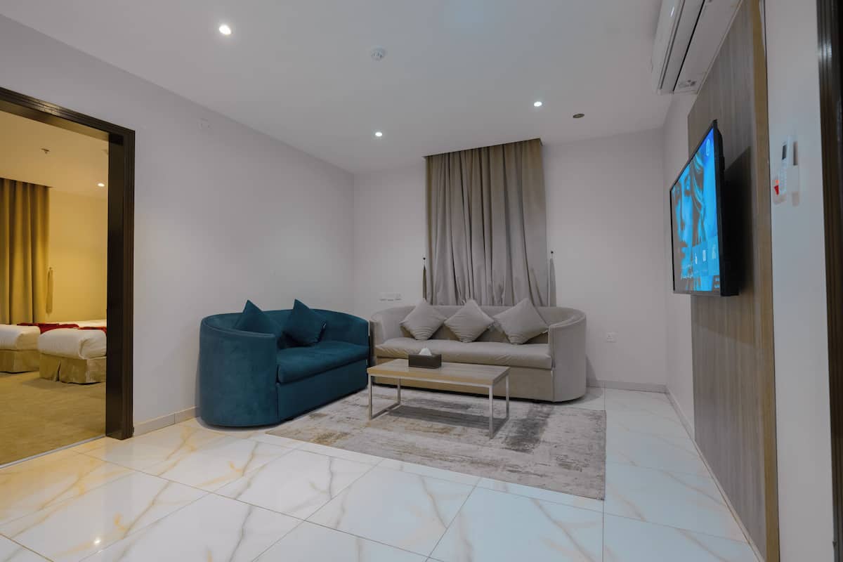 A modern living room with a sofa, a blue armchair, a coffee table, and a flat-screen TV mounted on the wall.