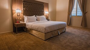 A hotel room with a large bed, two bedside tables with lamps, a wooden headboard, and a window with curtains. - Akarem Jazan Serviced Apartments (Jizan)