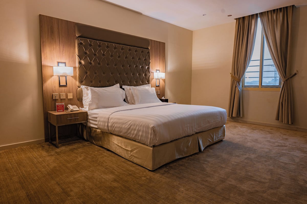 A hotel room with a large bed, two bedside tables with lamps, a wooden headboard, and a window with curtains.