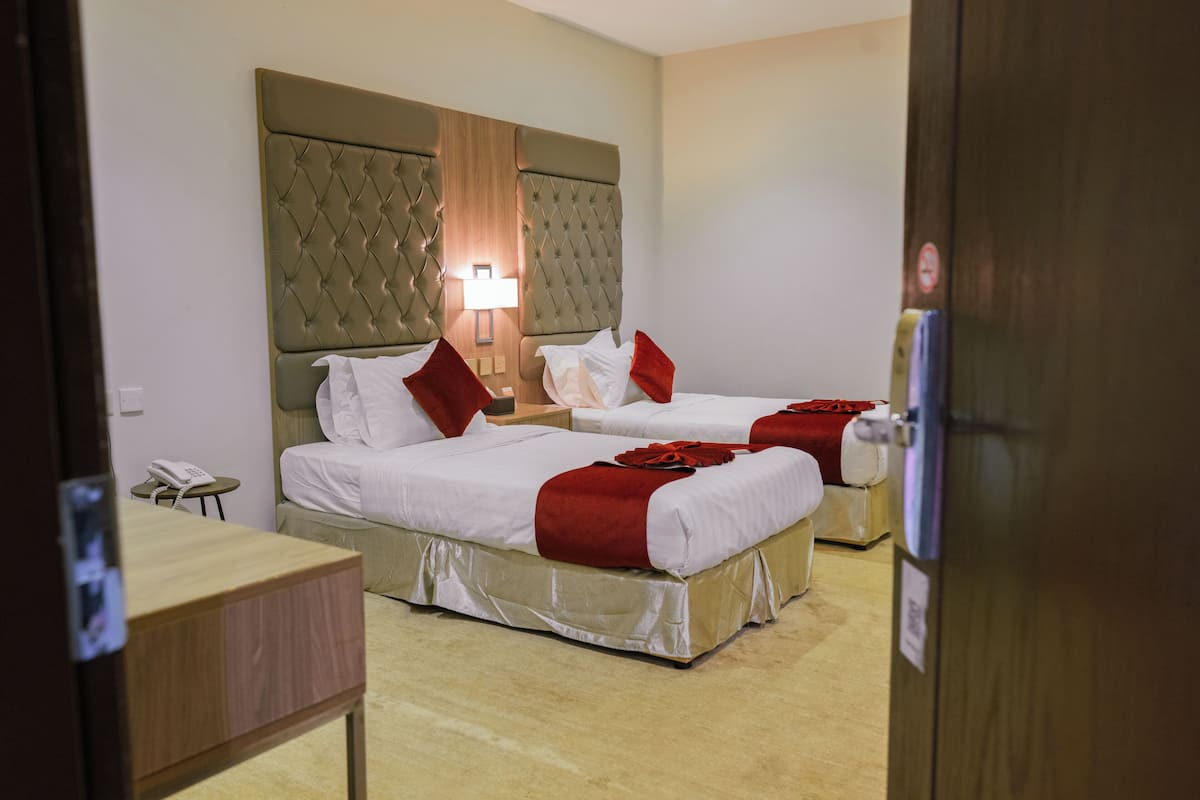 A hotel room with two beds, a bedside table, a lamp, and a telephone.