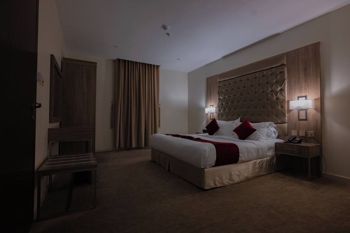 A hotel room with a large bed, two bedside lamps, a wooden headboard, a nightstand, and a door.