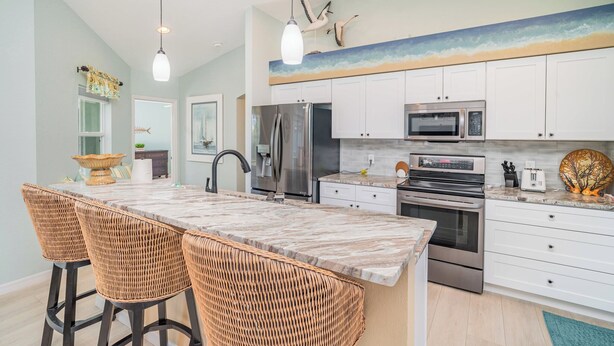 A modern kitchen with white cabinets, stainless steel appliances, and a large island with bar stools. - Sunset (Rotonda West)