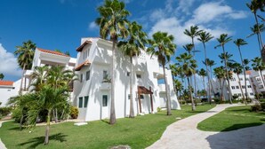 A white building with a red-tiled roof, surrounded by palm trees and a clear blue sky.