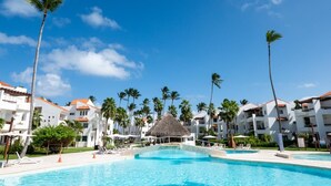 A resort with a swimming pool, palm trees, and white buildings with red roofs.