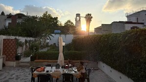 En tagterrasse med et bord og stole, omgivet af grøn vegetation og udsigt til et tårn i det fjerne.