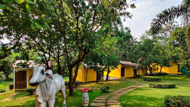 A courtyard with a statue of a cow, a yellow building, and a stone pathway. - RKS RESORT KARJAT (Karjat)