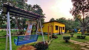 A playground with a slide and swings, a yellow building, and a well-maintained garden. - RKS RESORT KARJAT (Karjat)