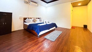 A bedroom with a bed, wooden flooring, a ceiling fan, and a small rug. - RKS RESORT KARJAT (Karjat)