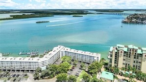 Un hotel frente al mar con un puerto deportivo, varias construcciones y un puente al fondo.