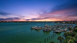 Un puerto deportivo con barcos amarrados, rodeado de agua y un horizonte urbano al fondo.