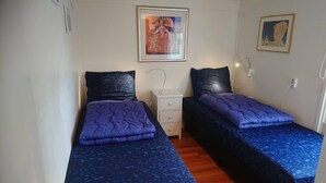 Una stanza con due letti, ognuno con una coperta trapuntata blu e cuscini neri. Si nota un piccolo comodino con una lampada e un cassetto.