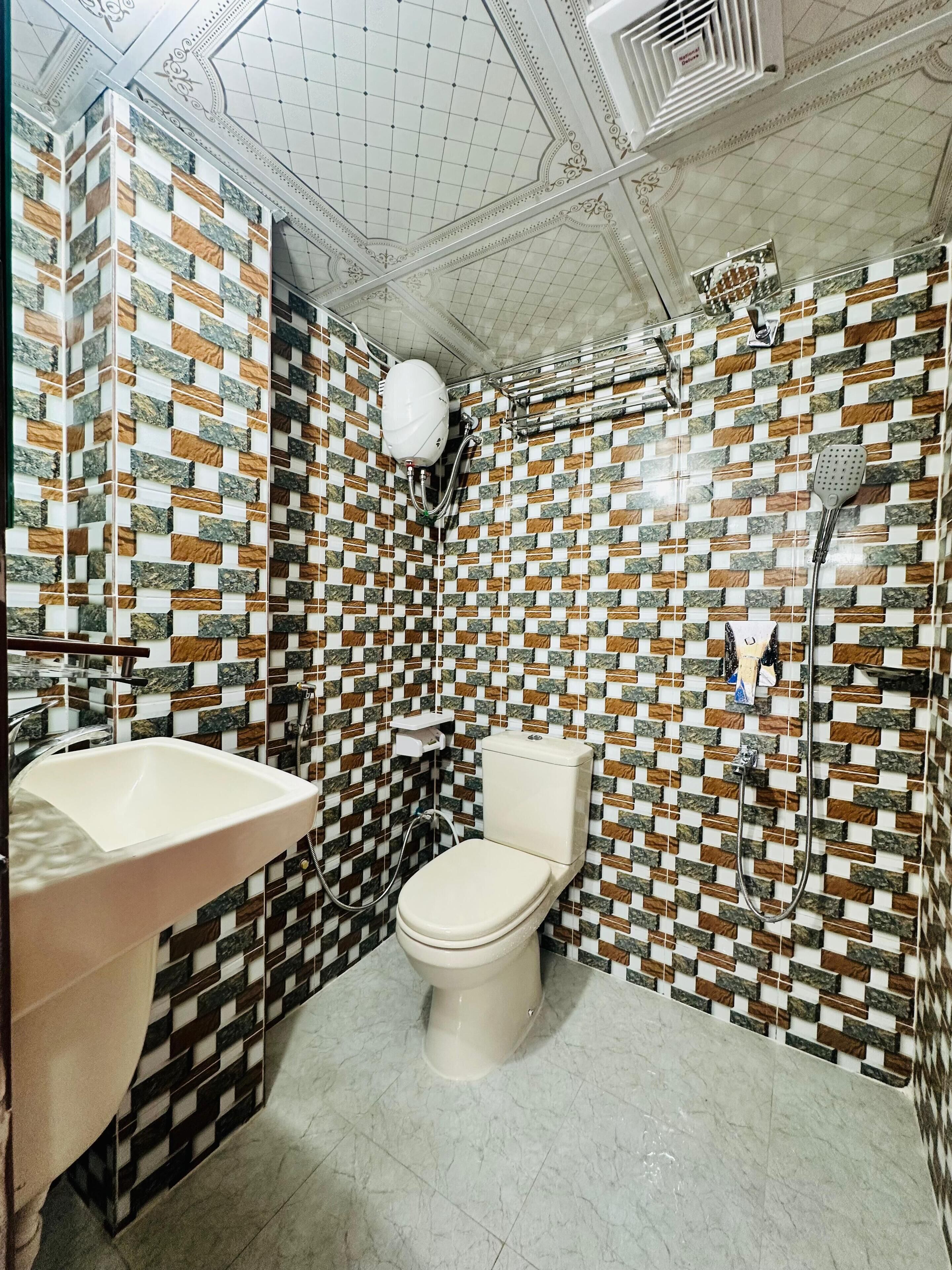 Une salle de bain avec un mur carrelé, des toilettes, un lavabo et une douche.