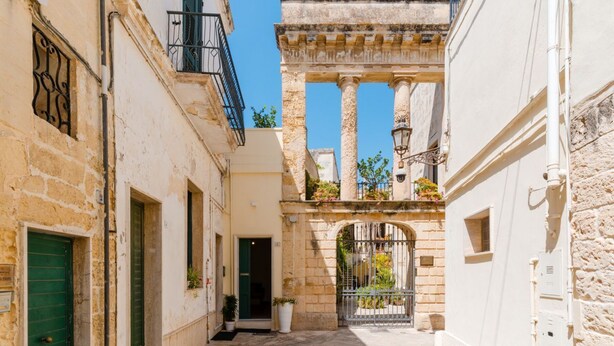 A narrow street with a building featuring a stone facade, a green door, and a balcony with potted plants. - Terrace Le Colonne - Lecce Selection (Lecce)