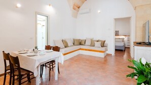 A dining area with a white table set for four, a sofa with cushions, and a stone arch ceiling. - Terrace Le Colonne - Lecce Selection (Lecce)