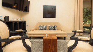 Una sala de estar con sofá, dos sillones, una mesa de centro, televisor de pantalla plana montado en la pared y una ventana con cortinas.