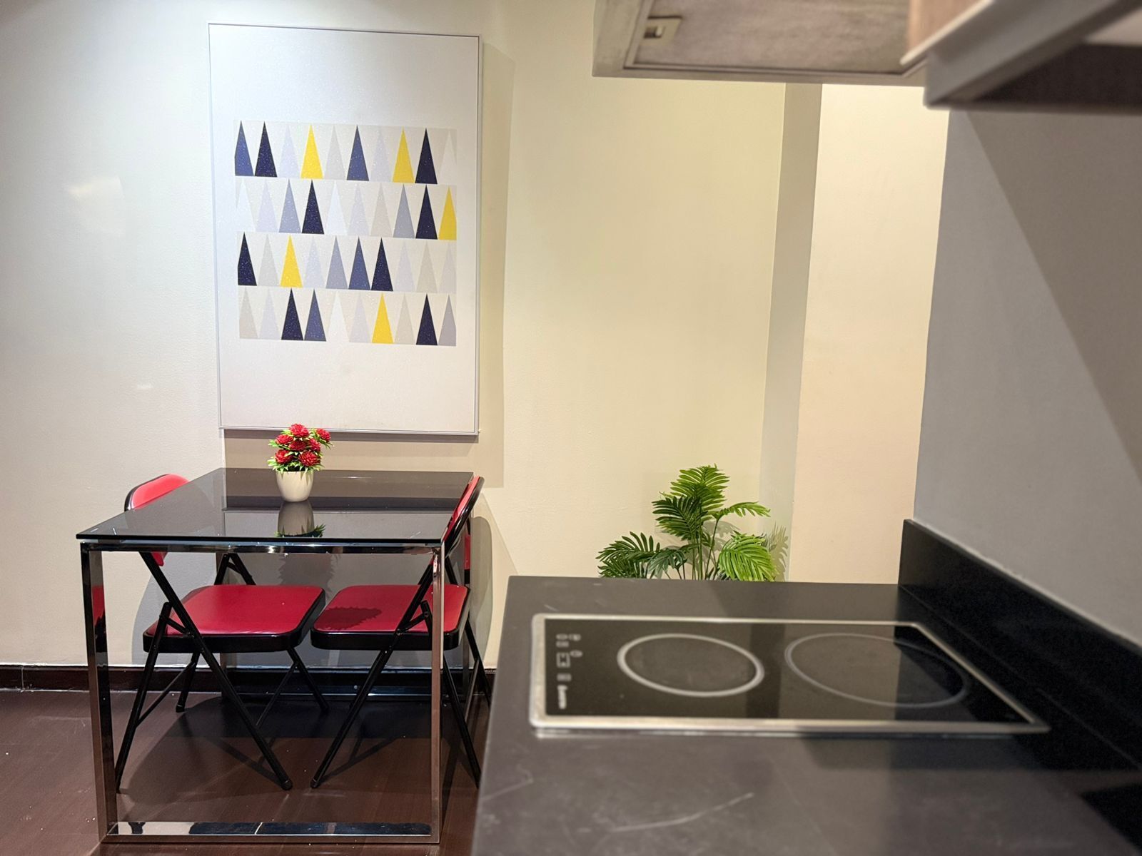 A compact kitchen with a black countertop, a built-in stove, and a dining area with a glass table and red chairs.
