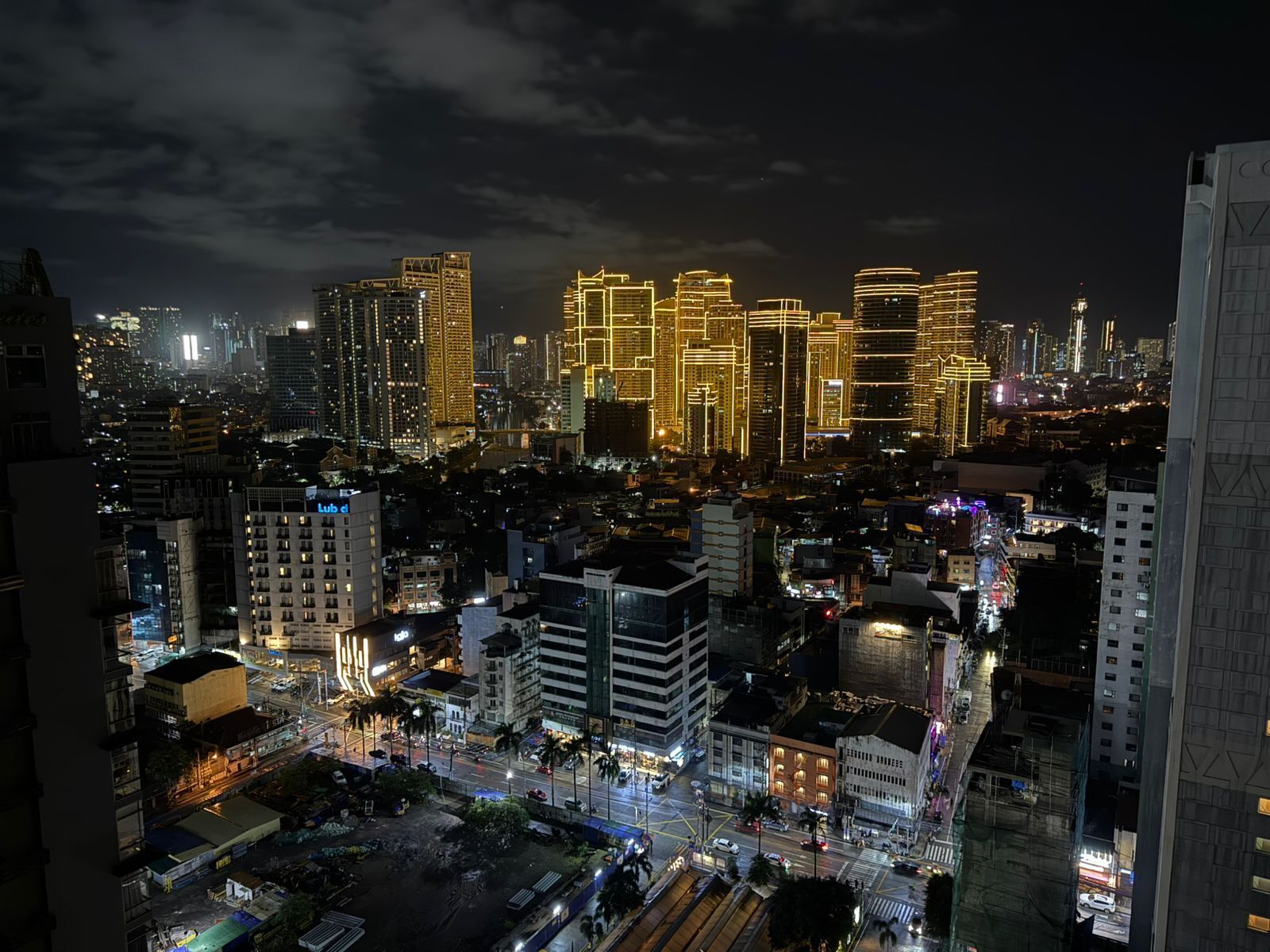 Panorama nocturno de una ciudad con imponentes rascacielos iluminados y una calle concurrida abajo.