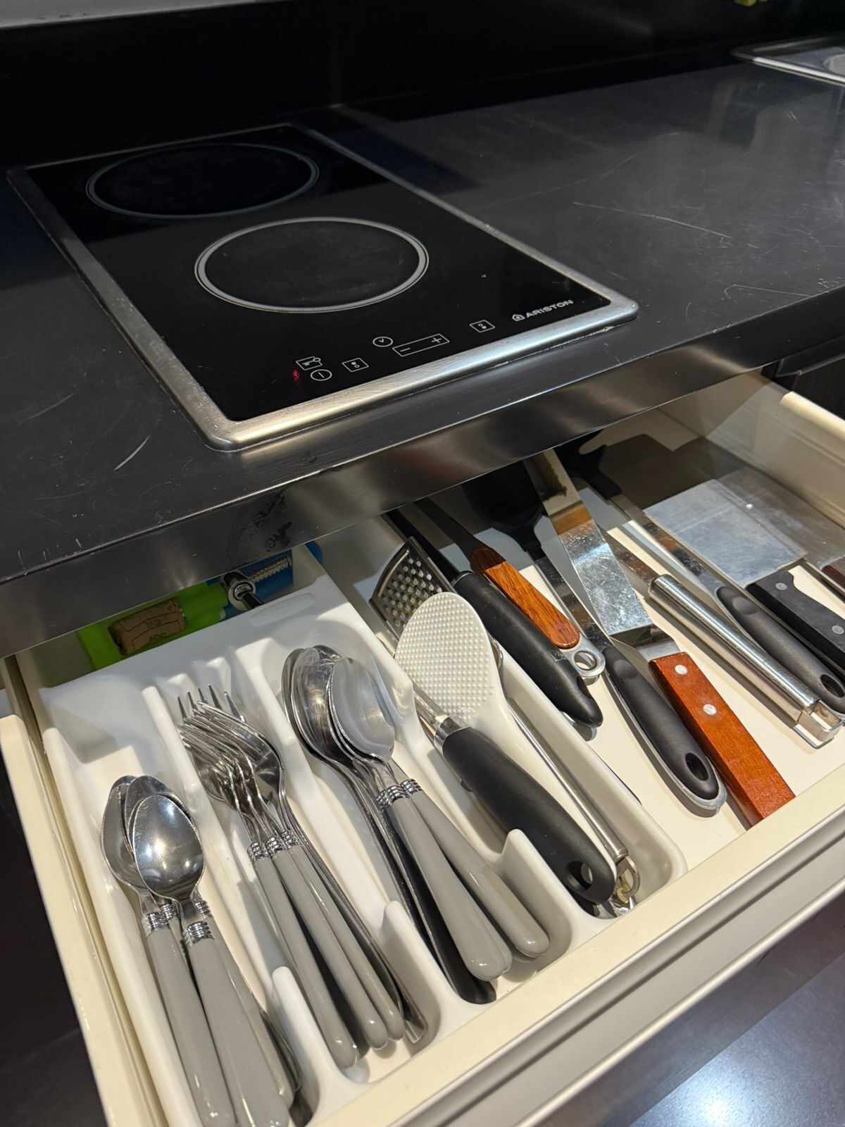 A drawer containing various kitchen utensils including spoons, forks, knives, and a grater.