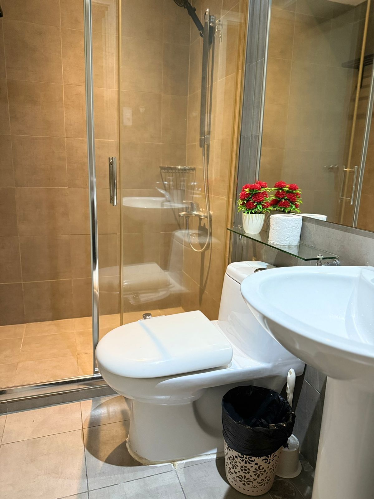 A modern bathroom with a glass-enclosed shower, a white toilet, a sink, and a trash bin.