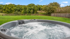 Un bain à remous dans une cour verdoyante, entouré d’une clôture en bois et avec des arbres en arrière-plan.