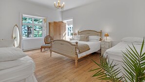 Une chambre avec un grand lit, deux tables de chevet, une chaise, une armoire et une fenêtre donnant sur des arbres.