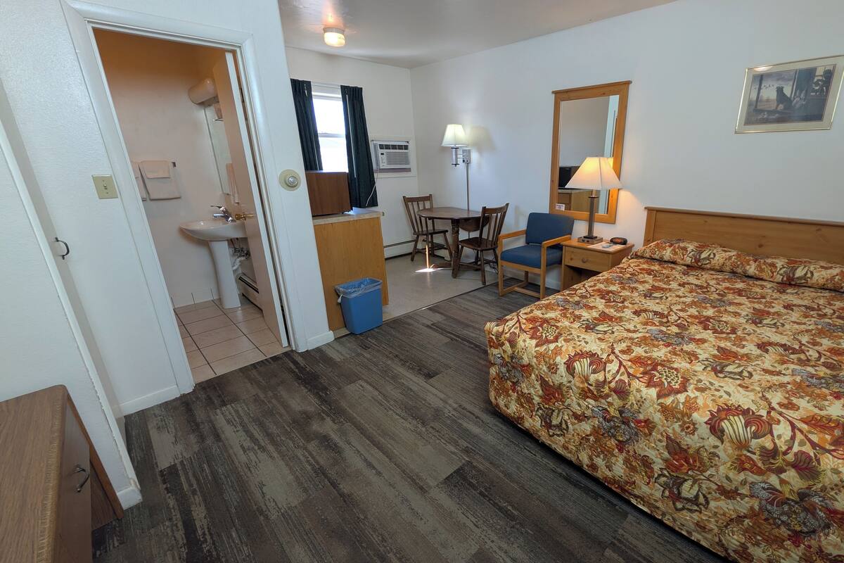 Une chambre d’hôtel équipée d’un lit, d’un bureau, d’une chaise, d’une petite table, d’un lavabo et d’un miroir.
