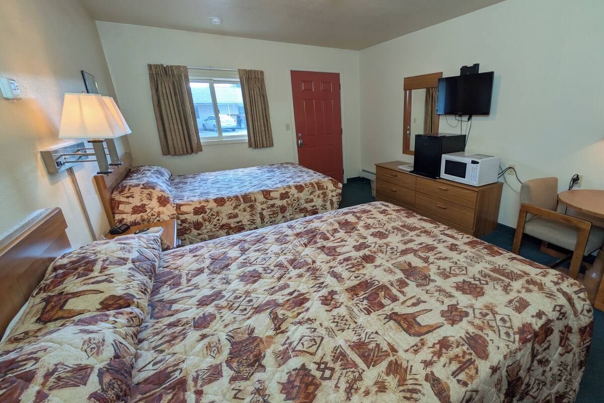 Une chambre d’hôtel avec deux lits, un bureau, une chaise, une télévision, un four à micro-ondes et une fenêtre avec des rideaux.