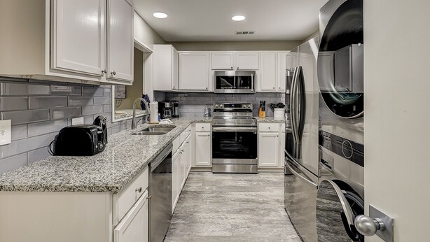 A modern kitchen with white cabinets, granite countertops, stainless steel appliances, and a tiled backsplash.