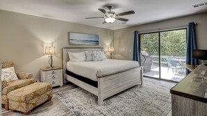 A bedroom with a bed, bedside lamps, a ceiling fan, a view of the outdoors, and a dining area with a table and chairs.