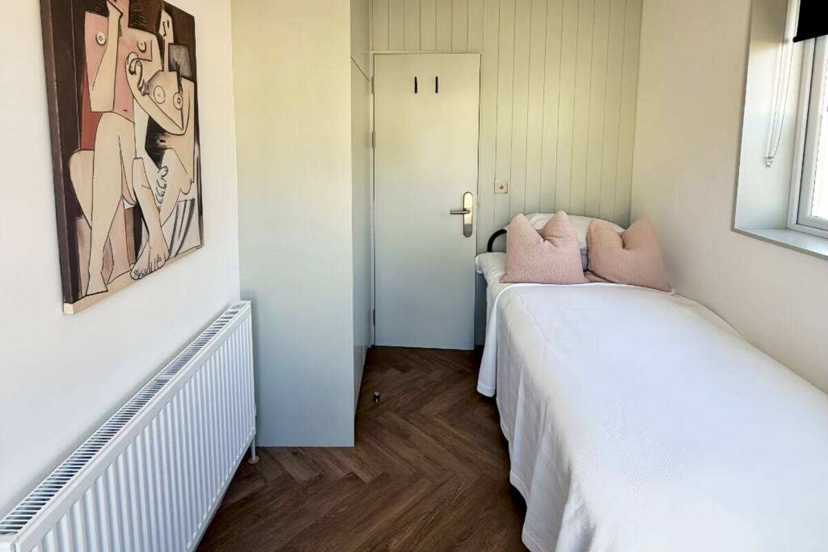 Une chambre à coucher comprenant un lit, un radiateur, une porte et une œuvre d’art accrochée au mur.