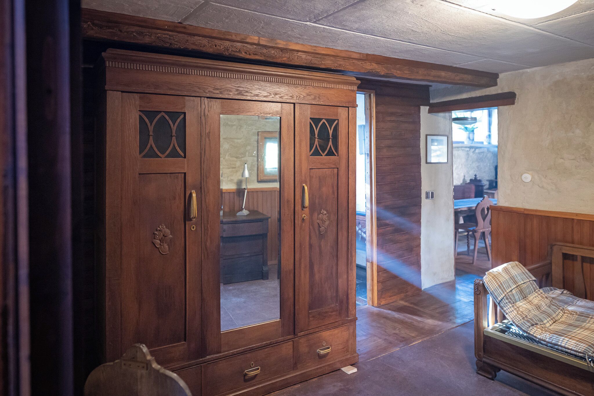 A wooden wardrobe with mirrored doors, a bench, and a dining area in the background.
