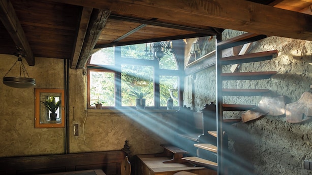 Une pièce rustique avec des bancs en bois, une table et une fenêtre laissant entrer la lumière du soleil.