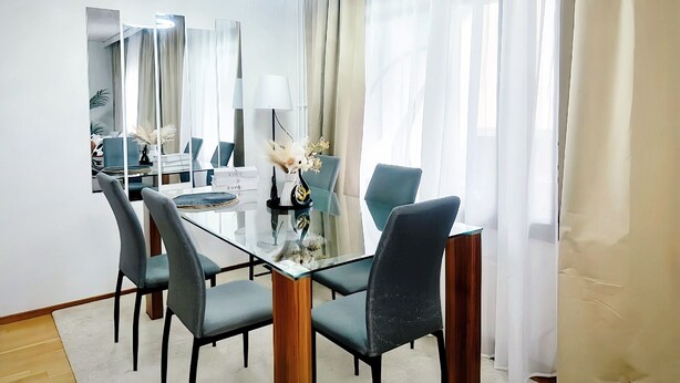 Et moderne spiseområde med et glasbord, fire stole, en vase med blomster og en lysekrone.