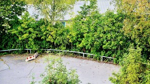 En anlagt flisebelagt plads omgivet af frodig beplantning, med gelænder og bænk.