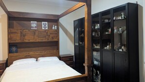 Un lit à baldaquin avec une tête de lit en bois, une commode noire aux portes vitrées et une petite table de chevet.