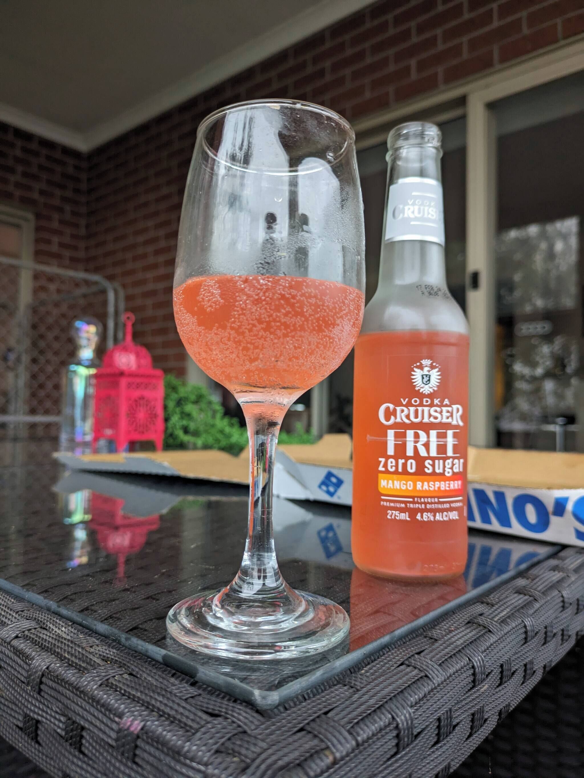 A glass of pink cocktail on a table with a bottle of Vodka Cruiser Free Zero Sugar Mango Raspberry flavor beside it.