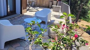 An outdoor patio with white furniture, a stone floor, and potted plants.