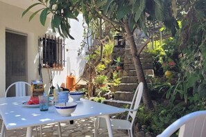 An outdoor dining area with a table and chairs, surrounded by lush greenery and a stone wall. - Between Land and Sea - A Quiet House in Rosamar (Canyet de Mar)