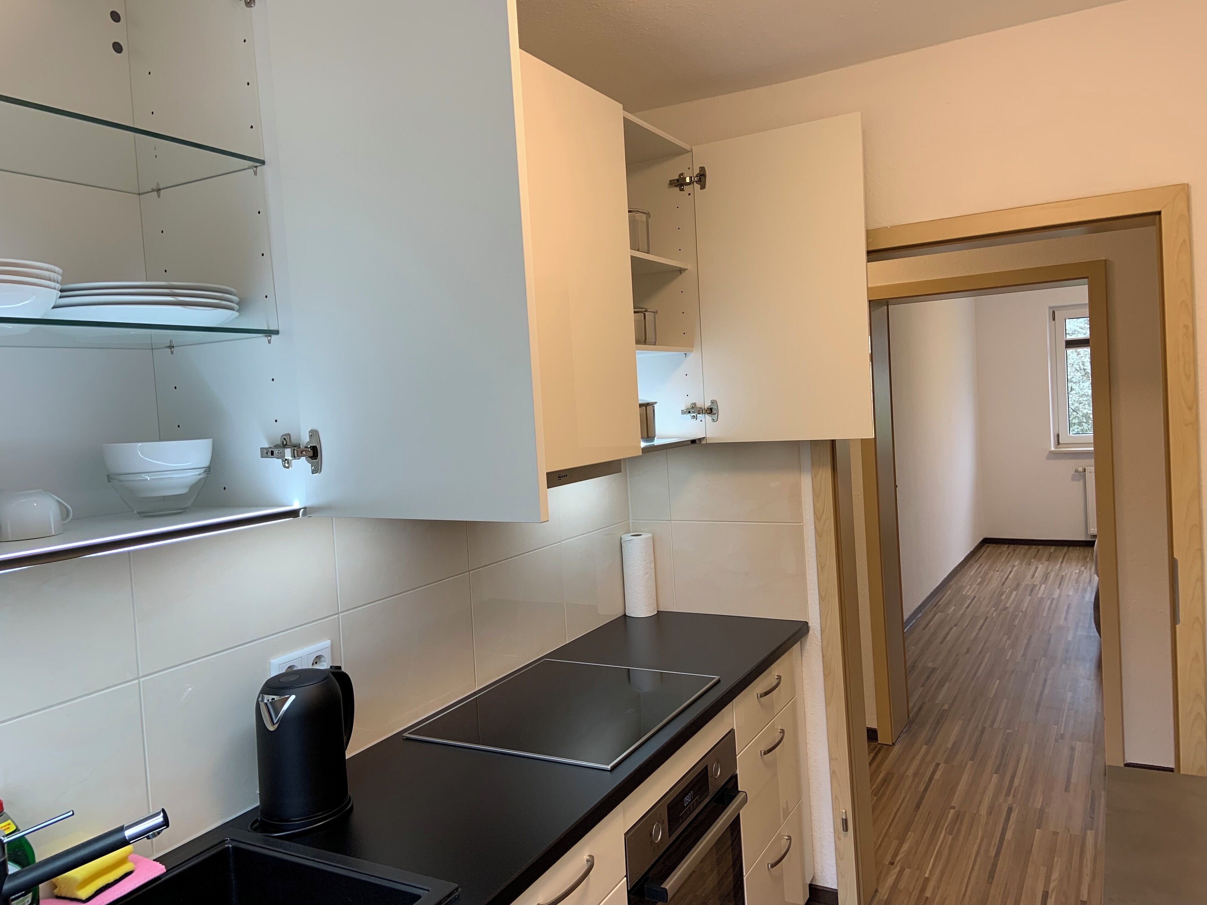 A kitchen with white cabinets, a black countertop, and a wooden floor.