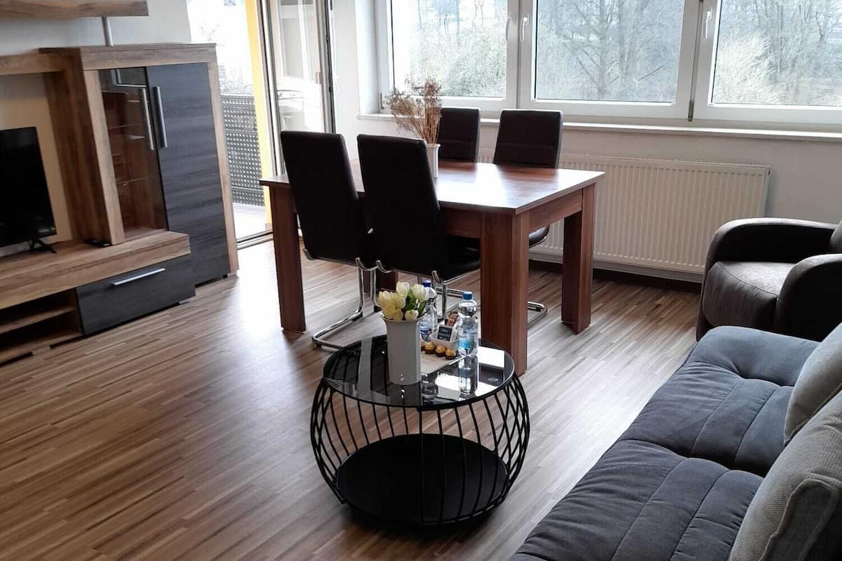 Un salon moderne avec un plancher en bois, une table basse ronde noire, un canapé gris et une table à manger avec des chaises.