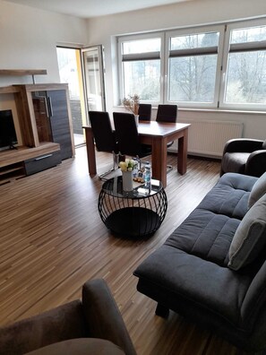 Un salon moderne avec un plancher en bois, une table basse ronde noire, un canapé gris et une table à manger avec des chaises.