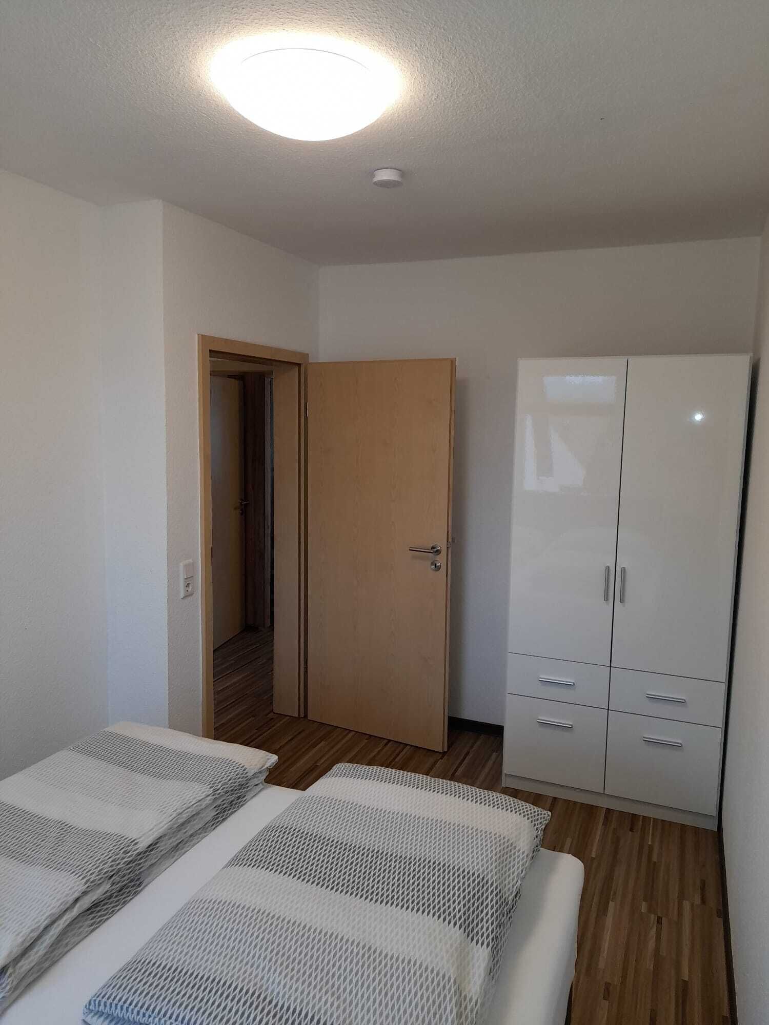 A room with a bed, a wardrobe, and a door leading to another room.