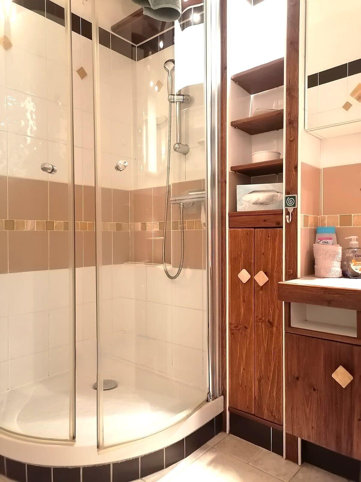 Un baño moderno con ducha acristalada, muebles de madera y suelo de baldosas.