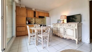 Una cocina con armarios de madera, una mesa de comedor con sillas, un televisor y una lámpara.