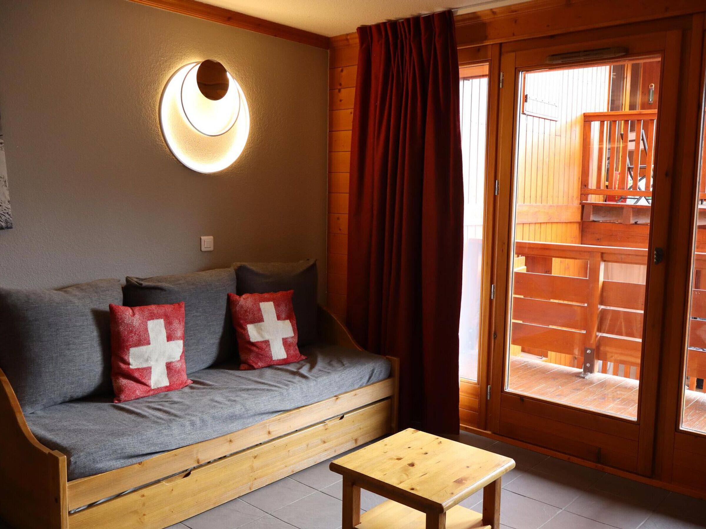 Un divano di legno con cuscini, un piccolo tavolino e una porta scorrevole in vetro che dà su una zona esterna.