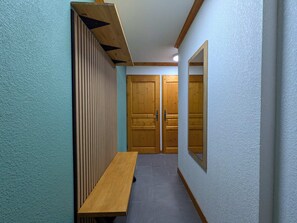 A hallway with a wooden bench, a wall-mounted mirror, and two wooden doors.