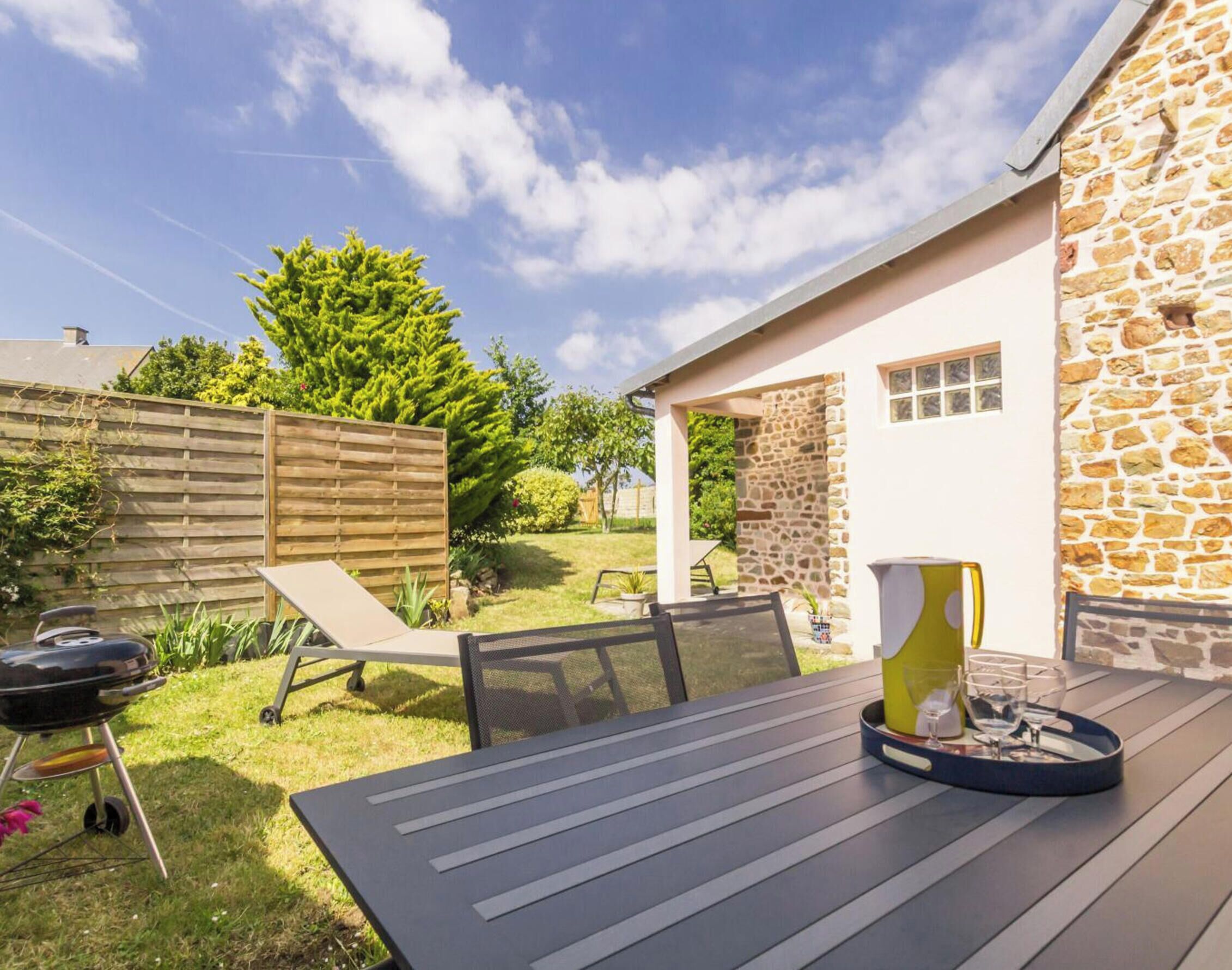 A patio with a table and chairs, a barbecue grill, and a stone wall.