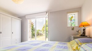 Une chambre à coucher comprenant un lit, une table de chevet, une lampe, une fenêtre ornée de vitraux et une vue sur l’extérieur.